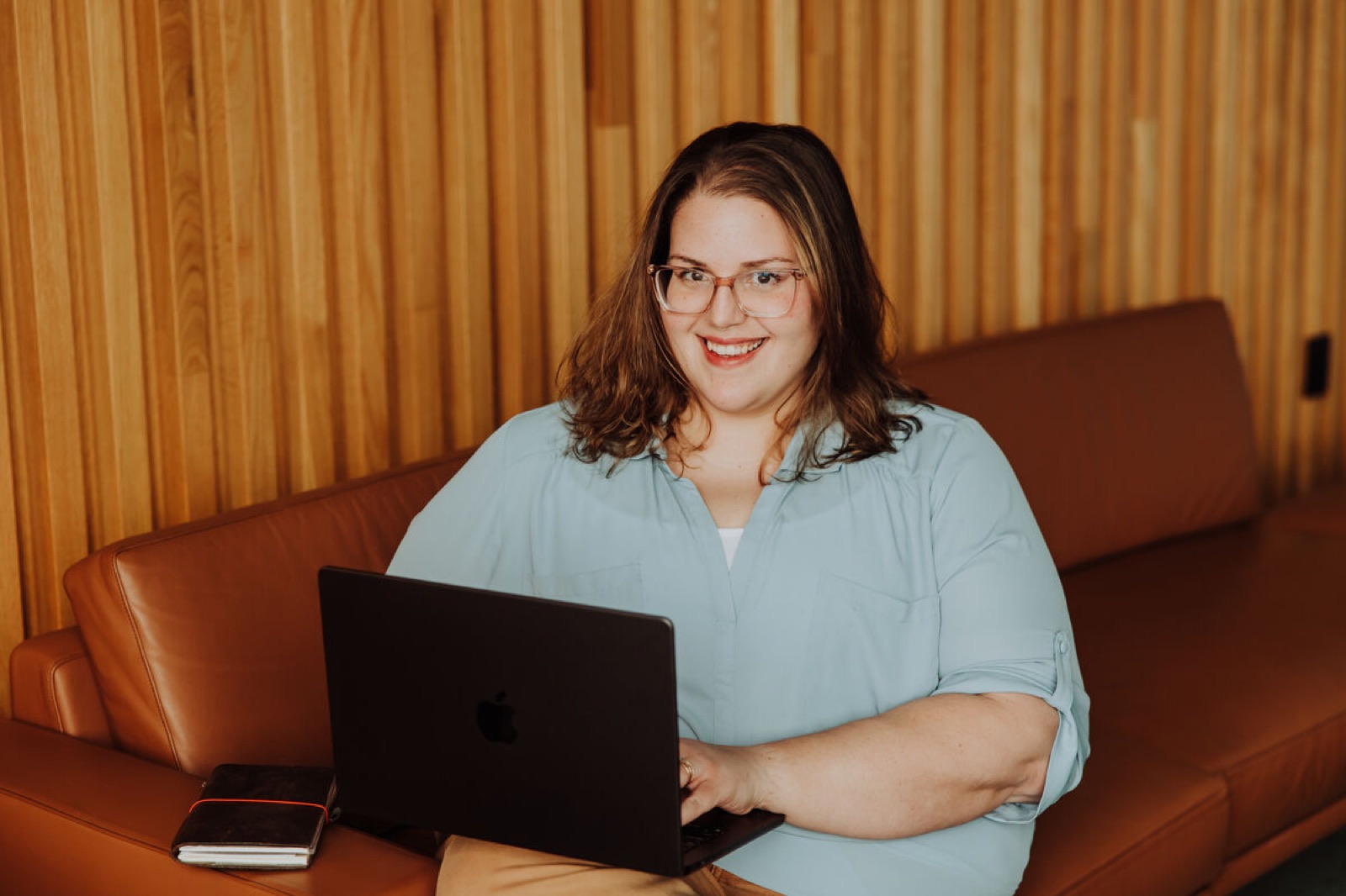 Jenn McGeehan smiling on a leather couch with her laptop